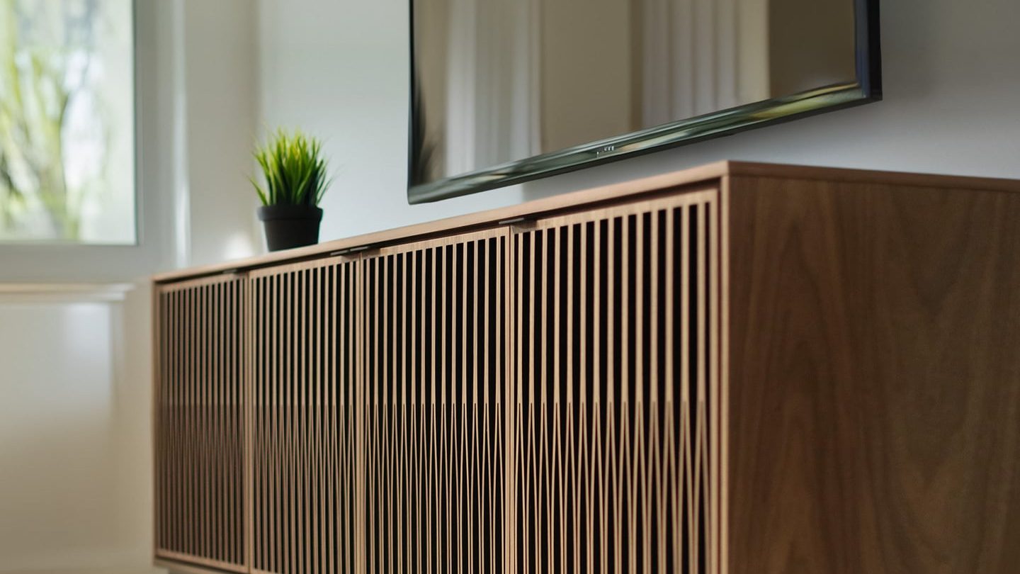 A clean and brightly lit living space is shown with an Elements 8703 media and storage cabinet by BDI Furniture, which has a rolling plinth base.  The Tune door pattern and washed oak finish are also featured.