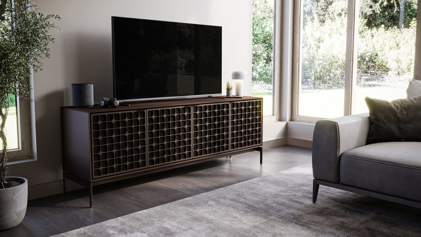The Elements modern TV stand and storage cabinet by BDI Furniture is shown with its acoustically transparent doors closed, a flat-screen television, and a Sonos speaker on top. It has a toasted oak finish and the Constellation precision-cut door pattern.