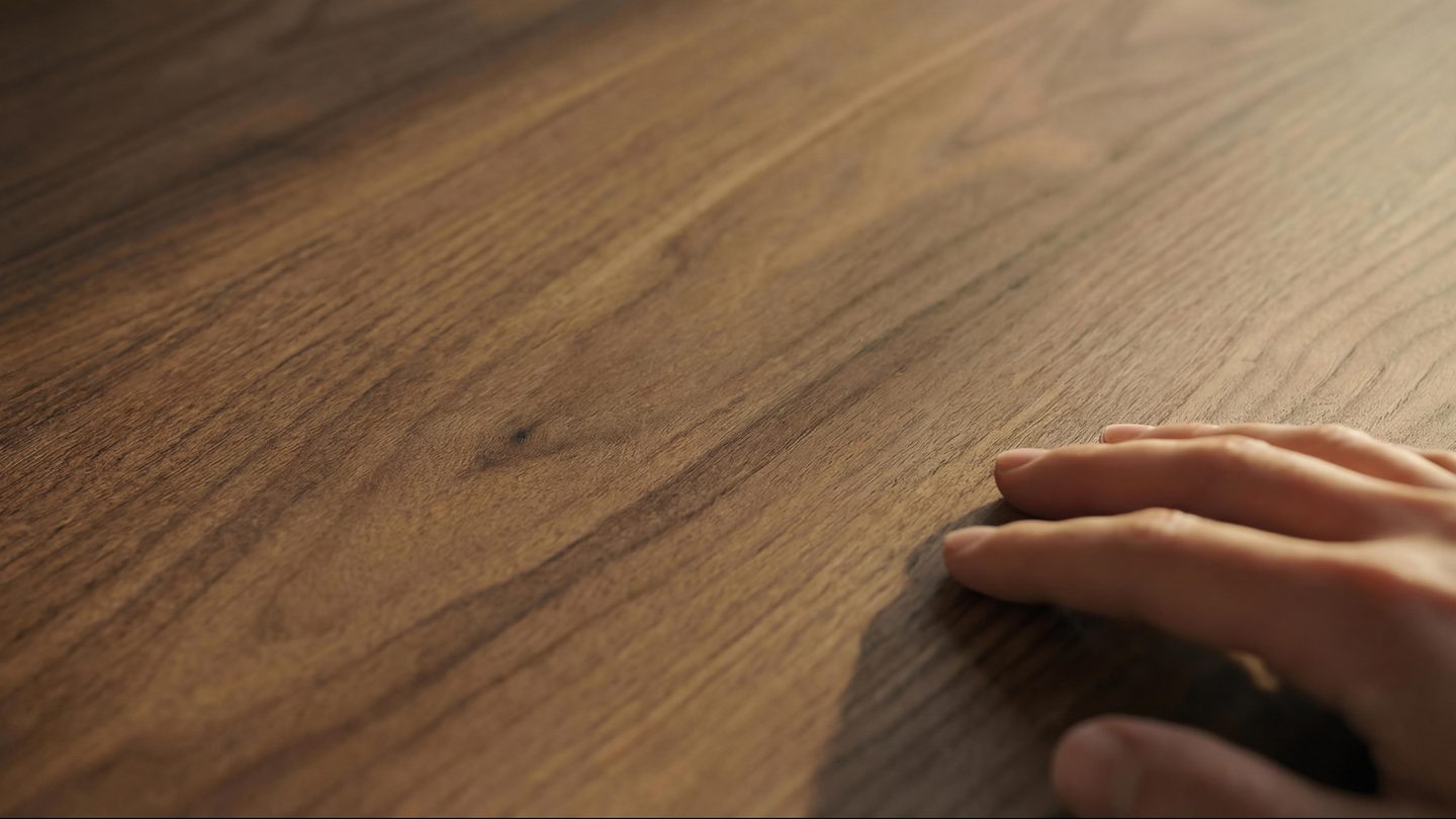 Close-up of a hand resting on a natural walnut wood surface, highlighting the grain and warm tones.