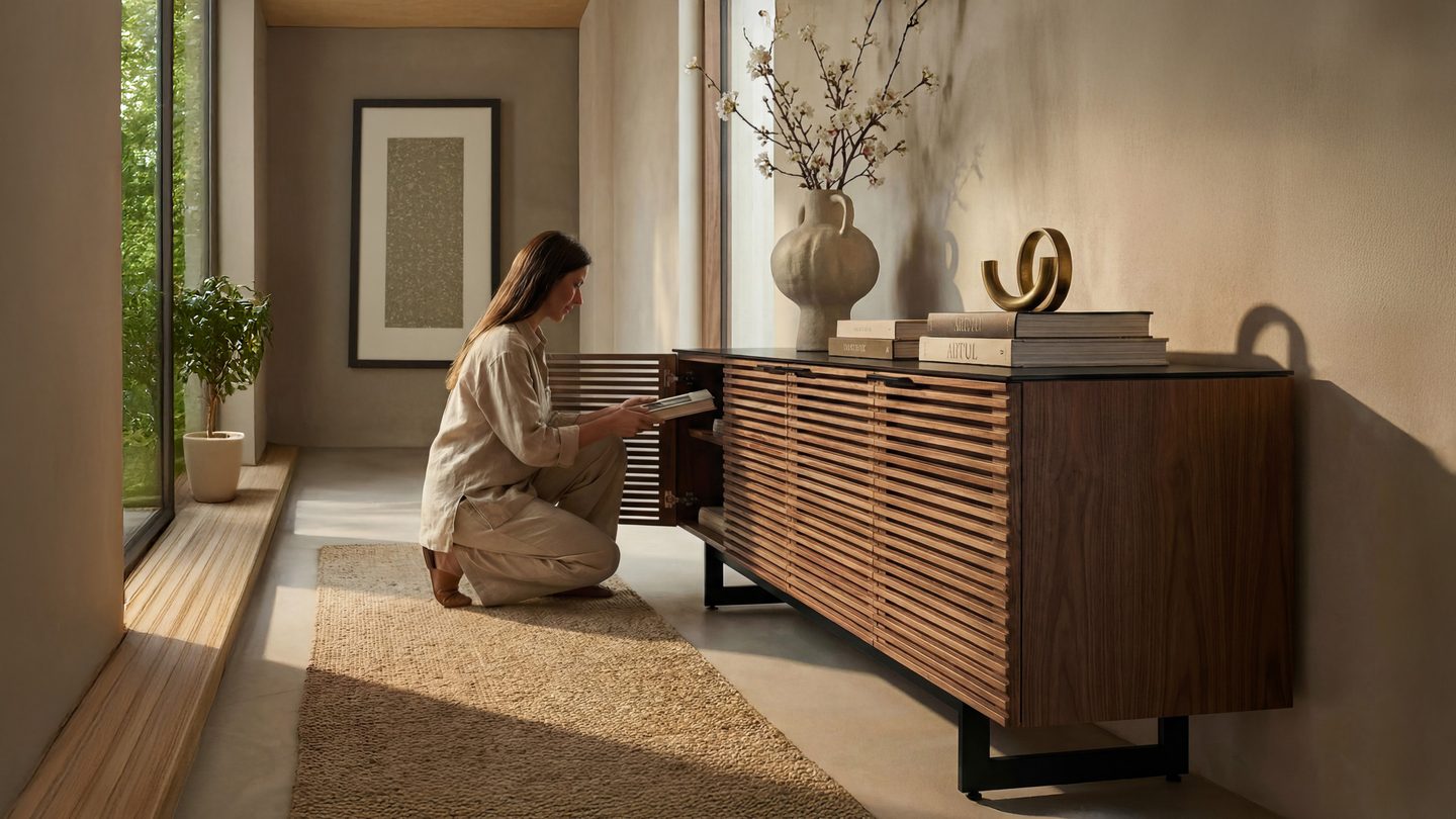 Person kneeling beside a BDI storage cabinet in Natural Walnut, opening a slatted / louvered door in a warm, modern living space.