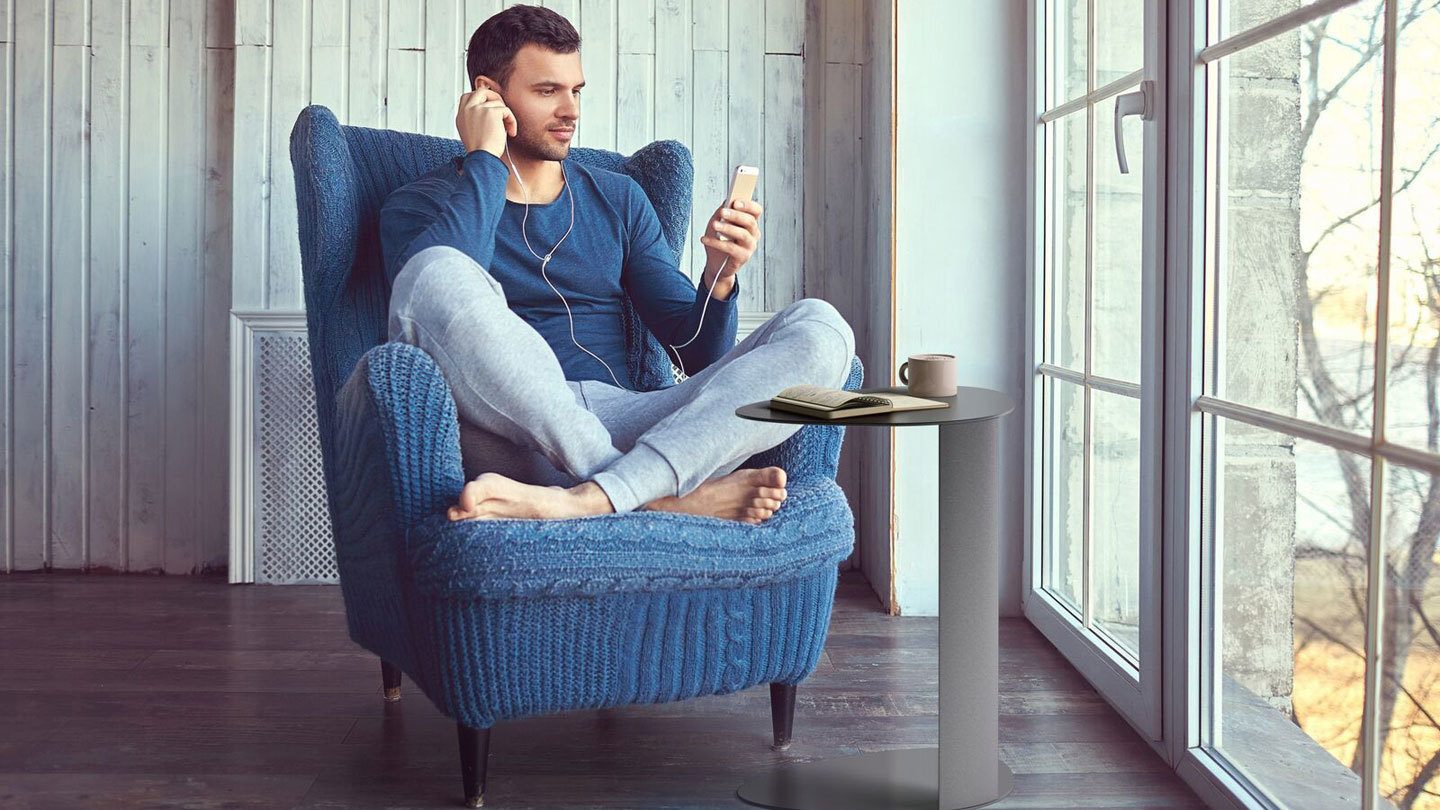 Millennial man sitting in a blue chair next to a Bink Mobile Laptop Table by BDI