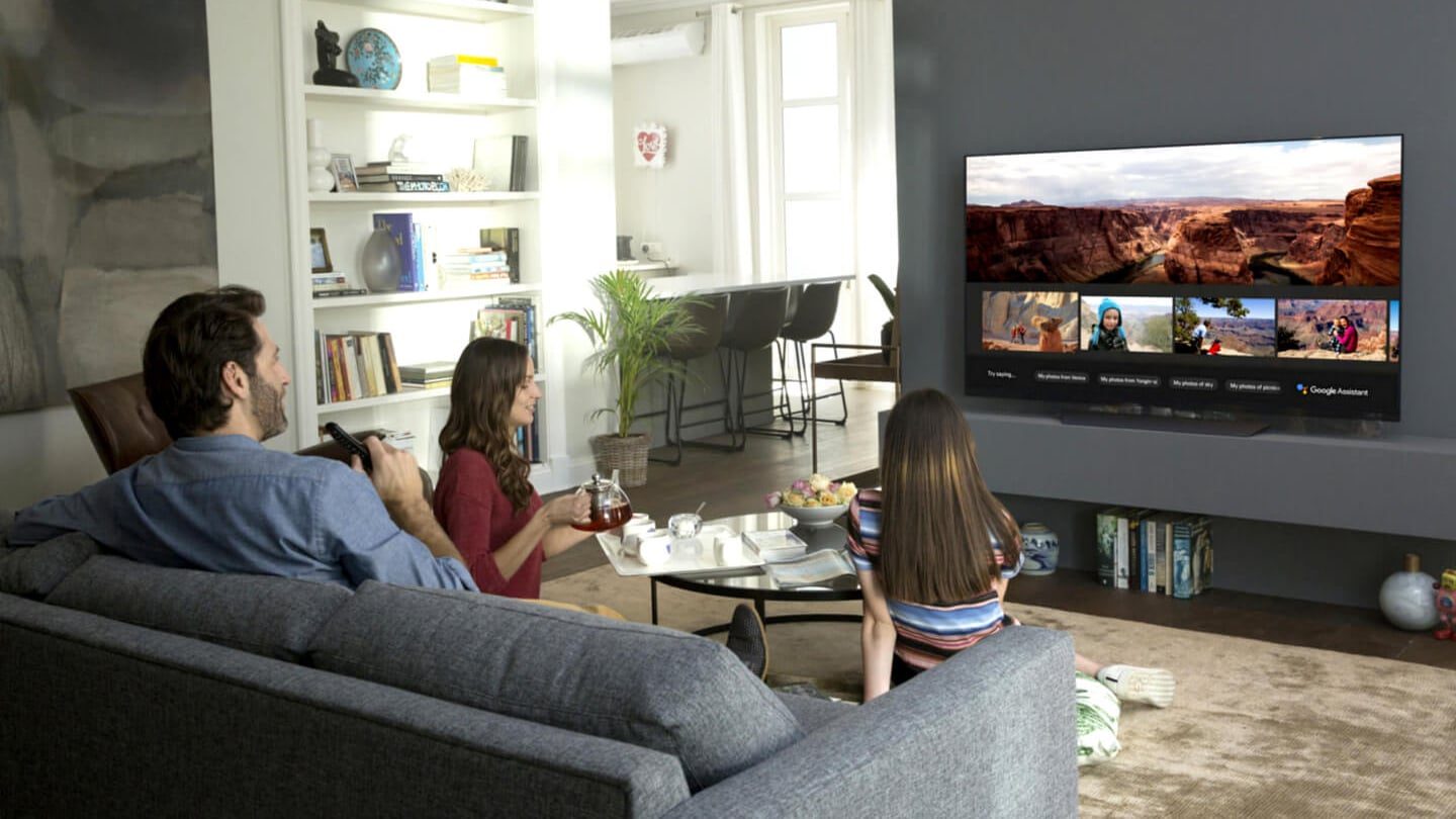 Family sitting on a couch in the living room watching television together.