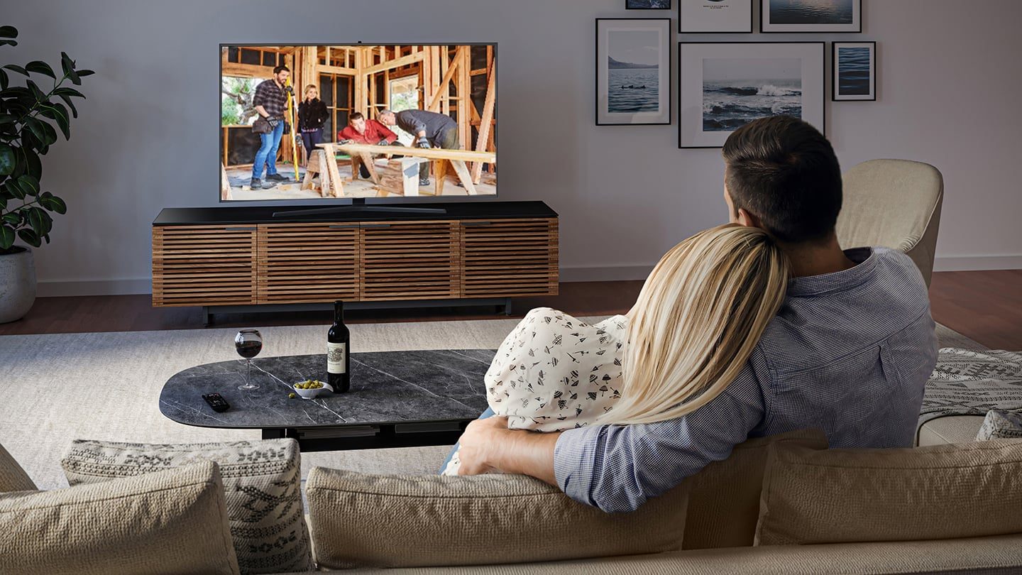 Couple sitting a couch in their new home, watching TV on a BDI Corridor 8179 TV stand in natural walnut finish.