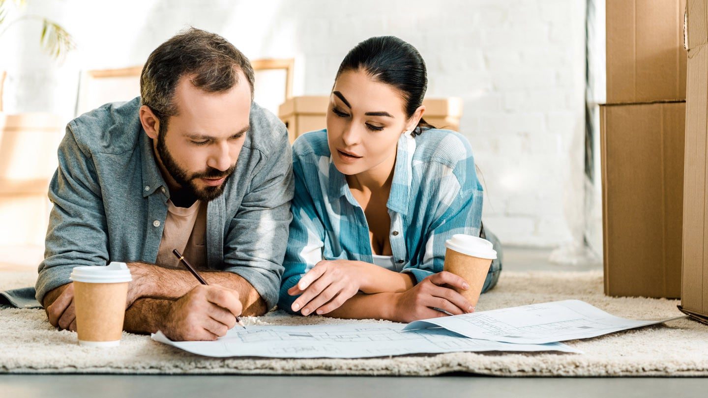 Couple laying on the floor of their new home, planning out their space and where to place their furniture.