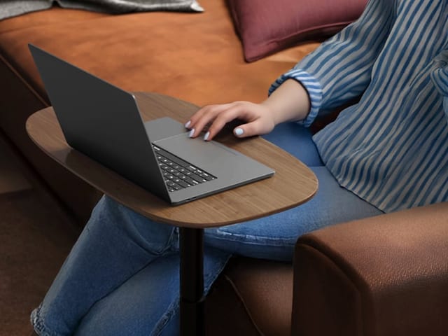 Serif 1046 Height-Adjustable Laptop Table by BDI in Walnut, shown in use by a woman sitting on a couch for ergonomic convenience.
