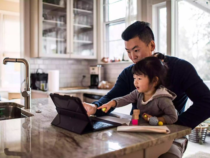 Millennial asian man, with his daughter, working from home in the family kitchen.